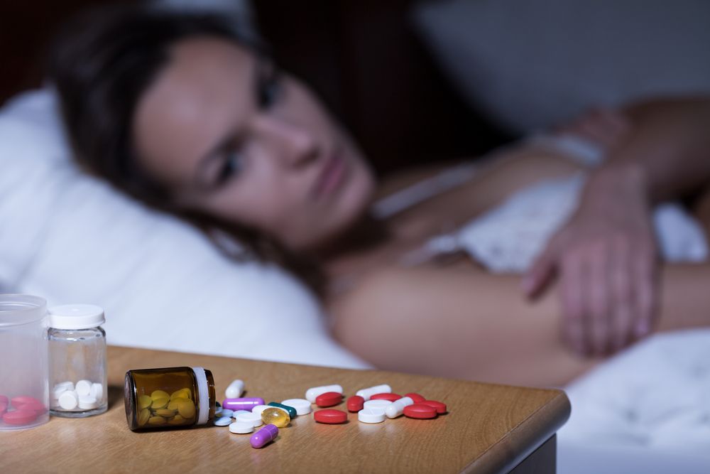 Sleeping pills on bedside table and awake woman