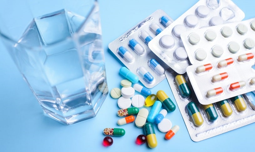 Colorful tablets with capsules near glass of water.