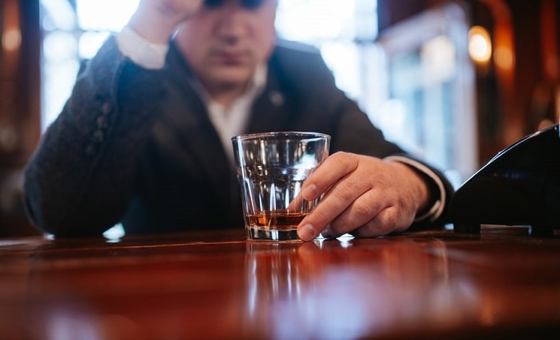 Man sits at a table with a bottle of alcohol.