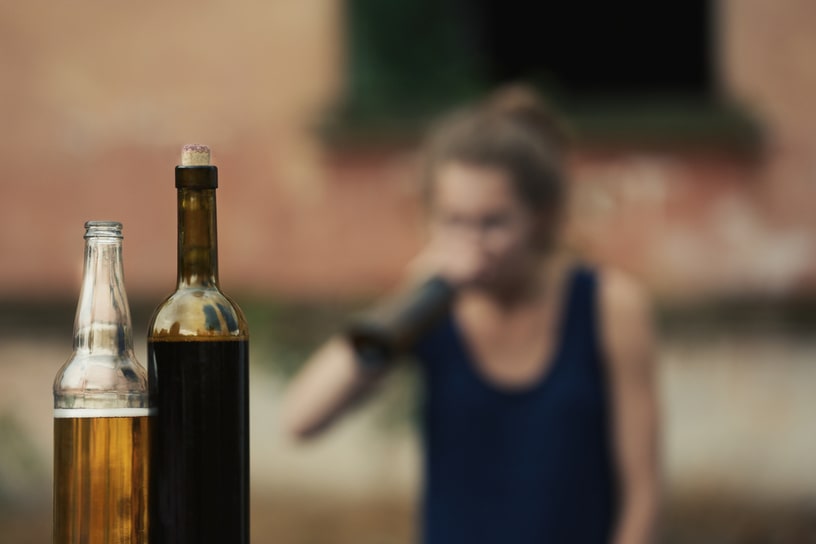 Bottles with alcohol stand against the background of a drinking woman.