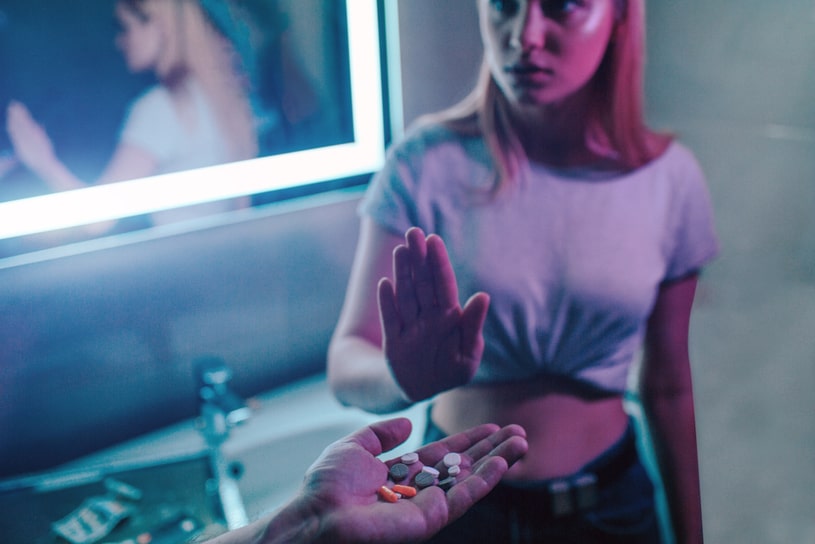The girl refuses a handful of pills that someone handed her in the greyish room.