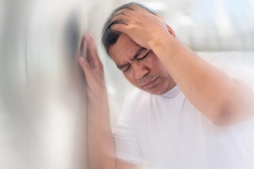 A middle-aged man feels dizzy while holding onto a wall with his hand.