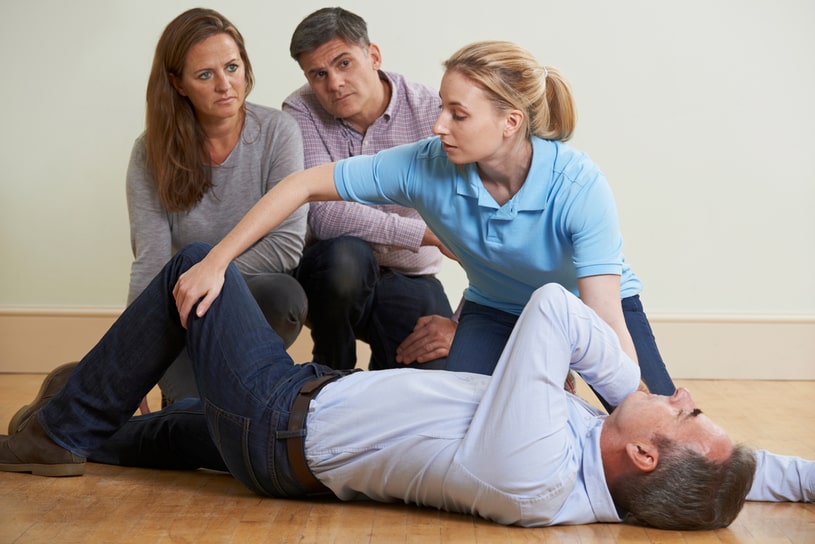A man is lying on the floor, and people around are trying to give him first aid.