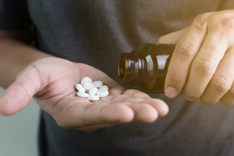 Male hand holding white pills in an open palm.