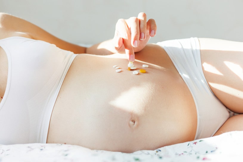 Pregnant woman in bed with many pills.