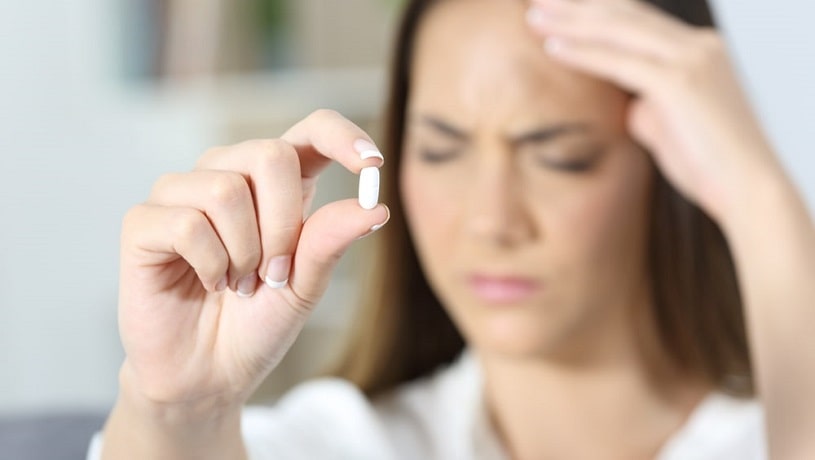 Woman suffering pain and holding a pill.