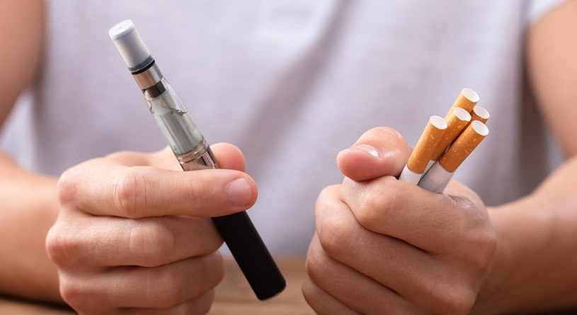 Woman holding a tobacco cigarette and an e-cigarette.