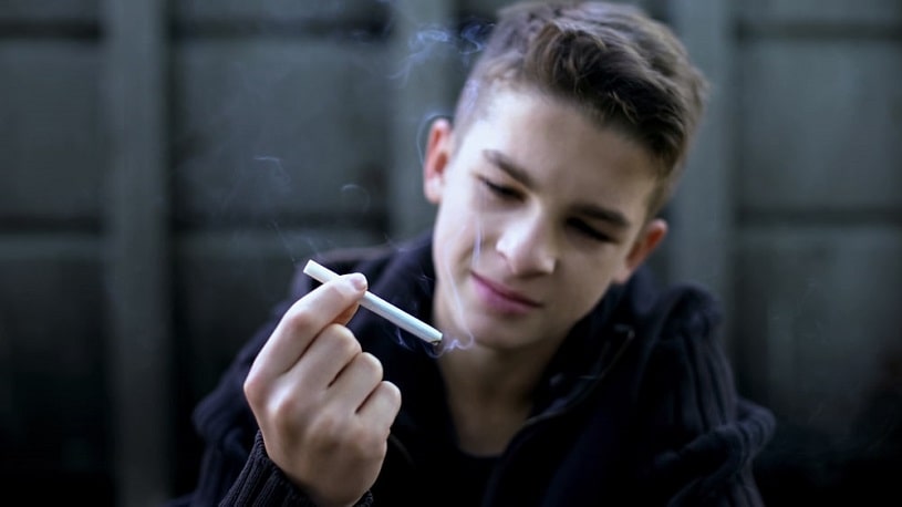 A teenages holding a cigarette smiling.