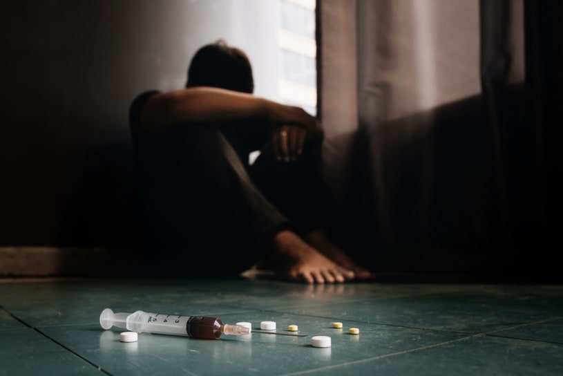 The depressed guy sits next to the pills and syringe.