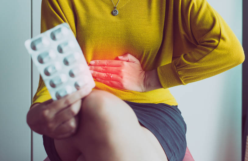 A woman is holding pills and has pain in stomach.