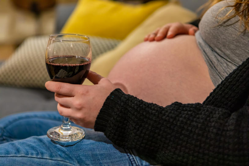 A pregnant woman with a glass of wine.