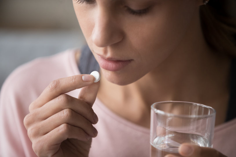 A woman takes Benadryl pills and holds a glass of water.