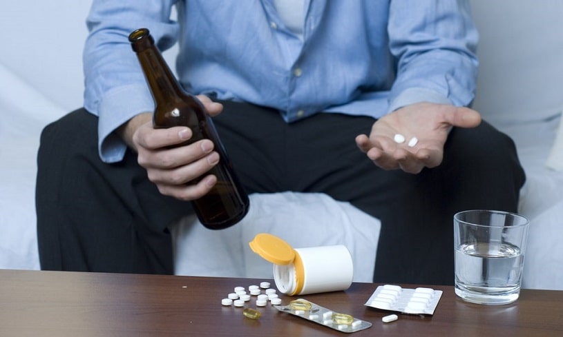 Man sitting on the couch with alcohol and blood thinners on the table and in hands.