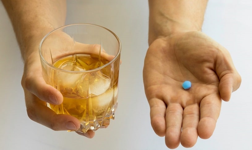 Close-up male hand holding viagra pill and glass with whiskey.