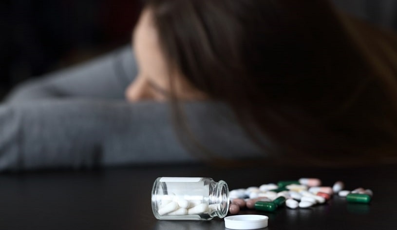 Woman lying after Klonopin overdose, many pills on the table.