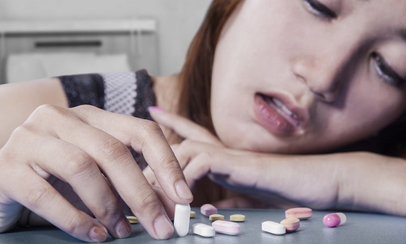 Sad woman addicted to Valium looking and touching pills.