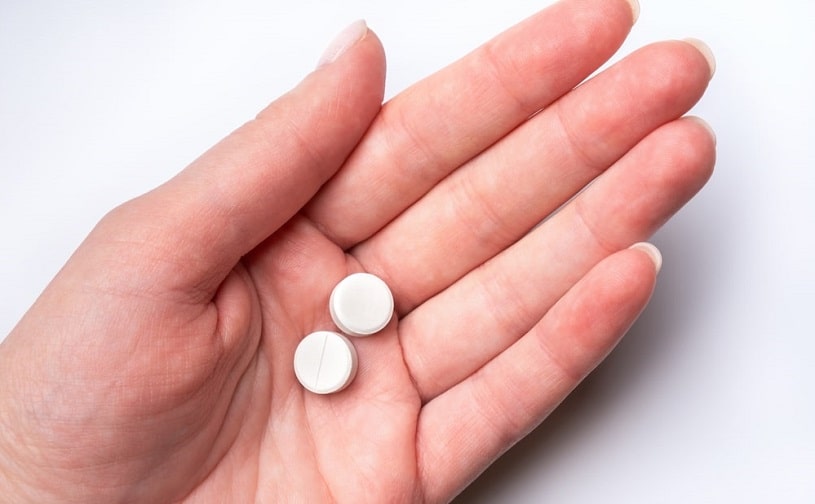 Female hand on white background holding two opioid pills.