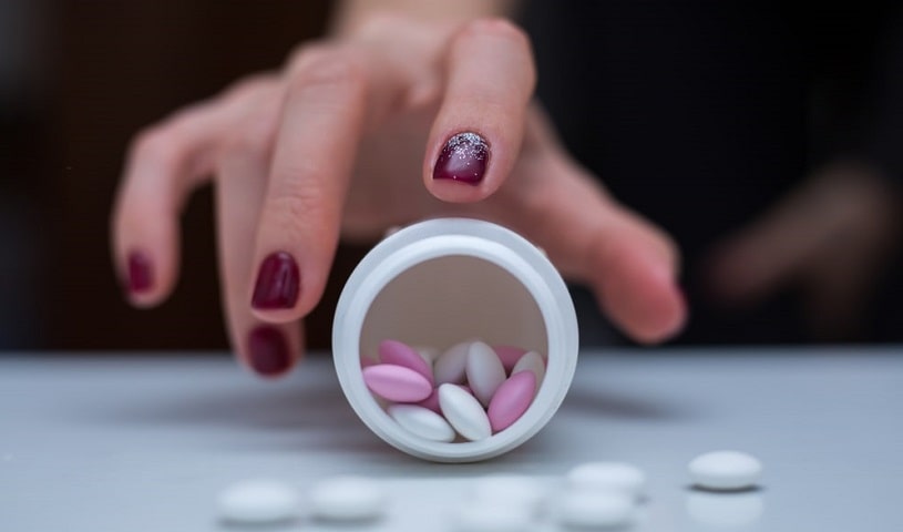 Hand with red nails surrounded by effexor pills.