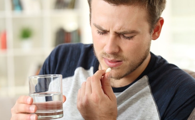 Man suffering and taking a pill on the sofa.