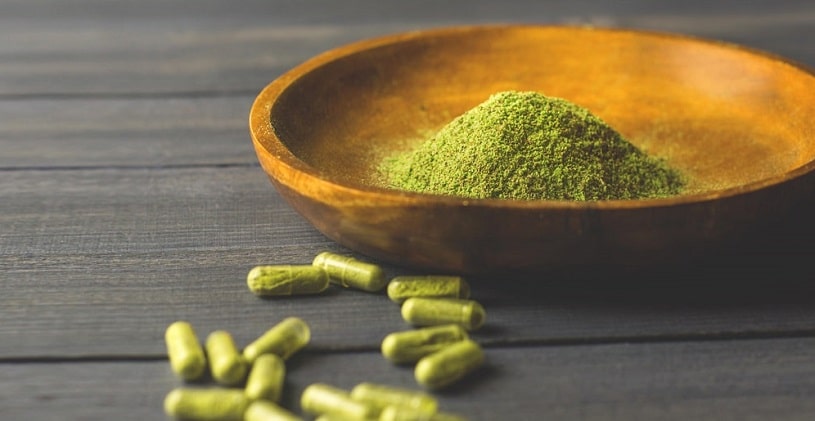 Green Kratom powder in a bowl and capsules.