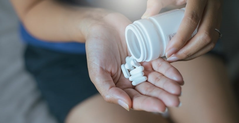 Woman spilling pills out of the bottle into a hand.