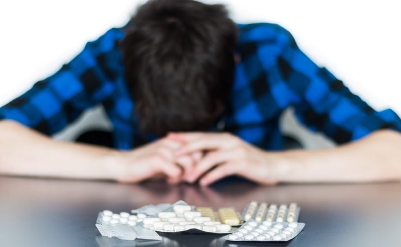 Young man sitting at the table with pills on the table.
