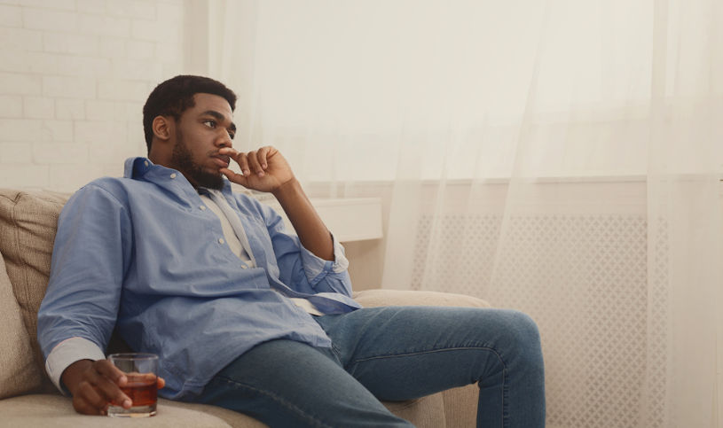 Depressed african-american man drinking alcohol at home.