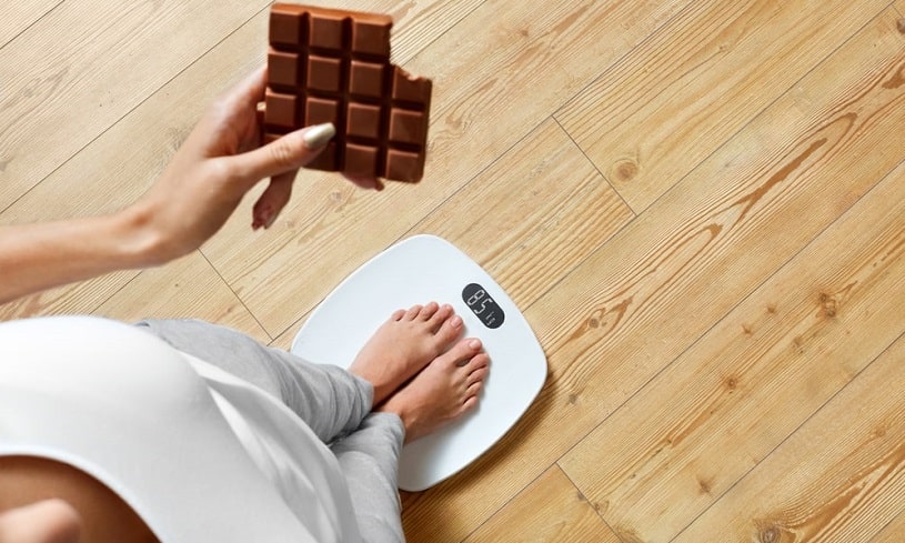 Woman with chocolate in hand worried about her weight.