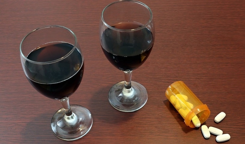 Two glasses of red wine next to bottle of Klonopin tablets.