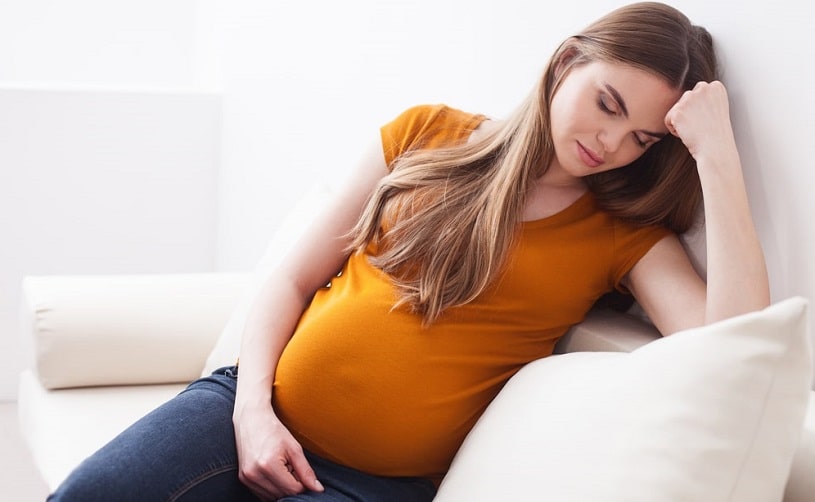 Pretty worried pregnant woman sitting on the couch.