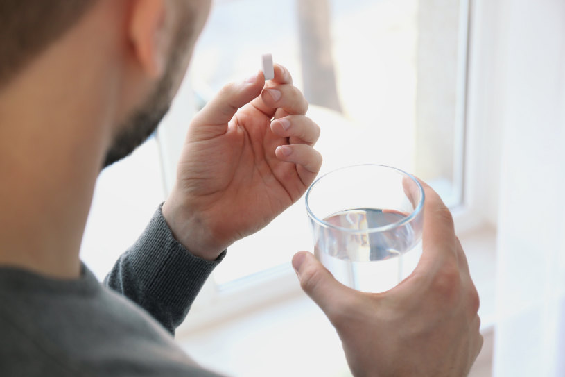A man holds a glass of water and drinks Phenazepam pills.