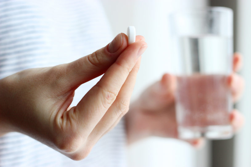 A woman holds Fiorinal pill in one hand and a glass of water in the other.