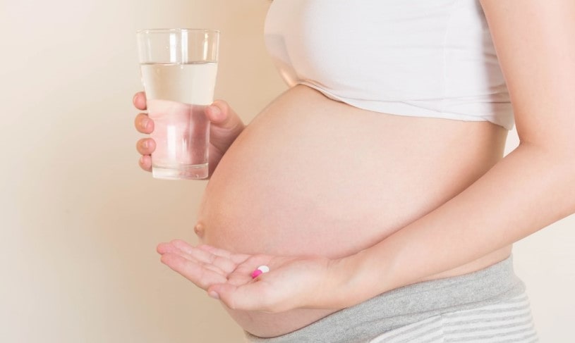 Pregnant woman holding a glass of water and Lortab 10 in another hand.