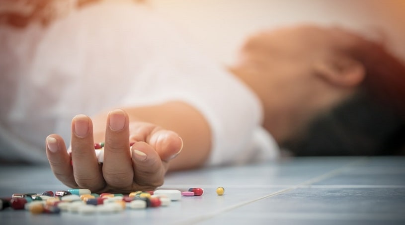Man lying on the floor next to many pills.