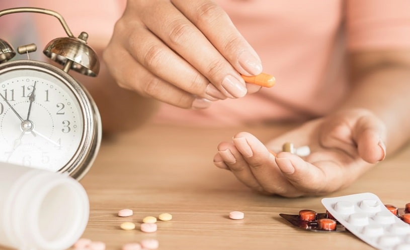 Woman hand taking pills with a glass of water.