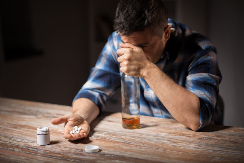 A man holds a bottle of alcohol and Amitriptyline pills.