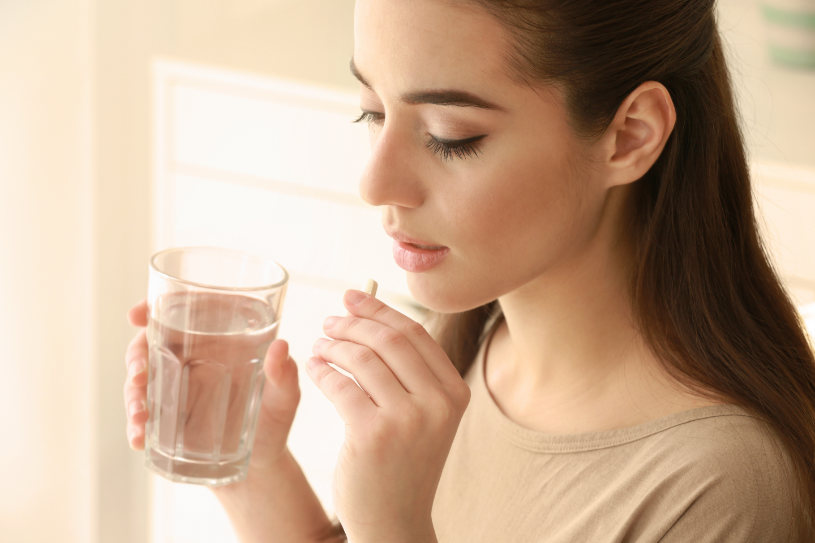 A woman holds a glass of water and a pill.