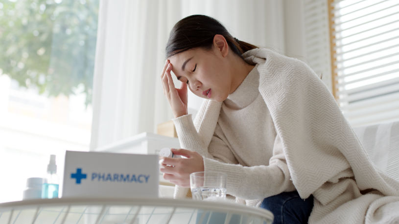 A woman is sitting on the sofa and experiences a headache due to Amitriptyline withdrawal.