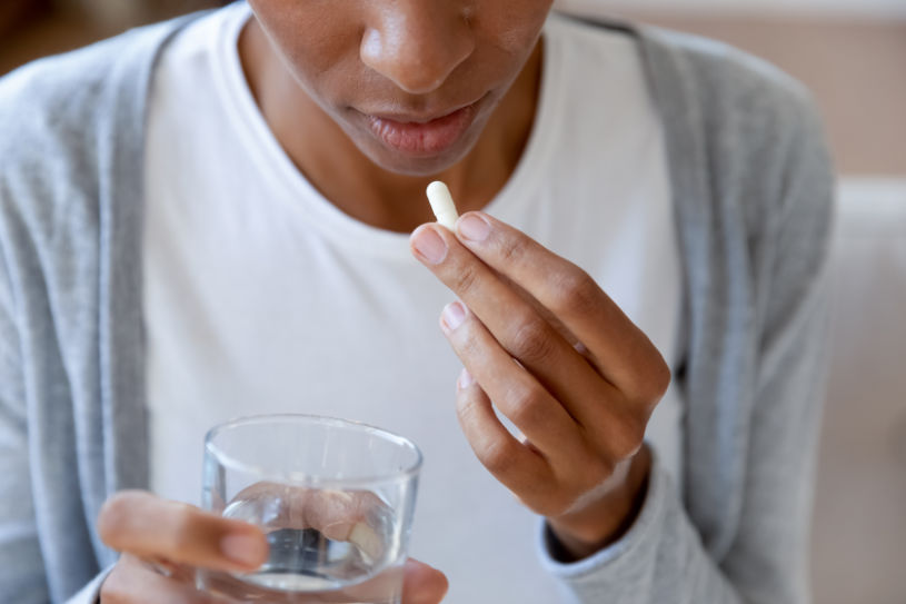 Close up of African American young woman feel sick drink antibiotic or antidepressant pill with water.