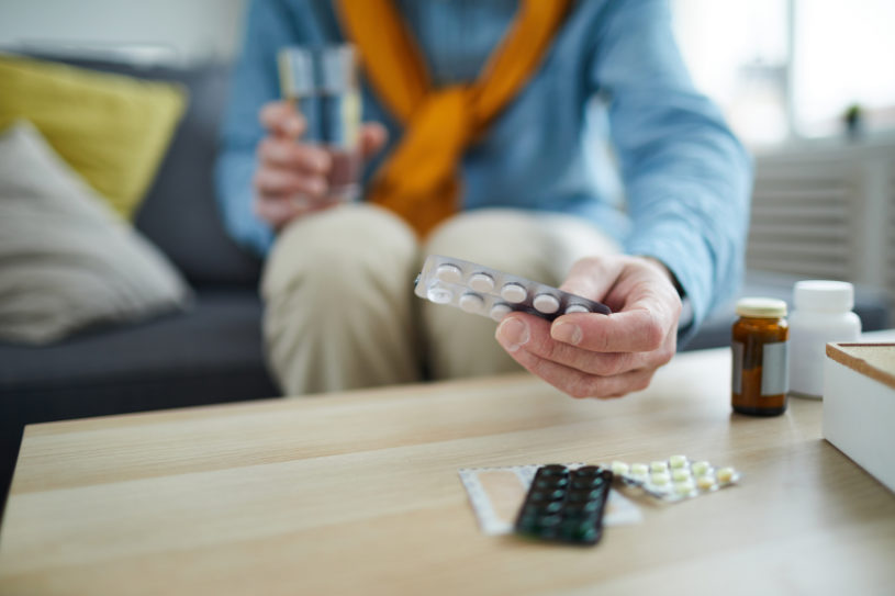 Closeup of unrecognizable senior man taking pills and medication off table at home.