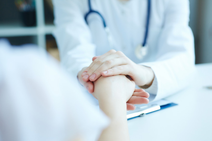 Friendly female doctor's hands holding female patient's hand for encouragement and empathy.