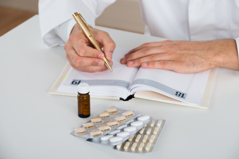 High angle view of doctor writing prescription at table in clinic.