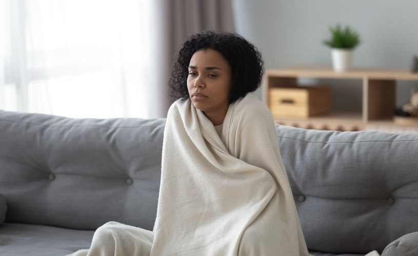 Woman covering with blanket sitting on the couch at home.