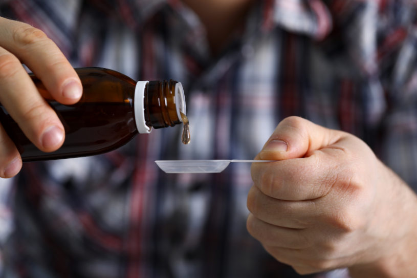 A man pours DXM cough syrup into a spoon.