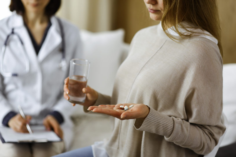 A woman holds a glass of water and DXM pills in her hand.