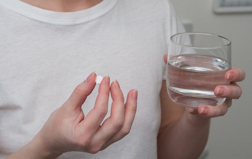 Woman taking a pill with a glass of water.