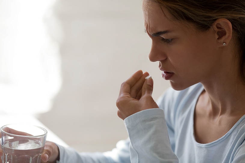 Unhappy woman in pain holds a pill and a glass of water.