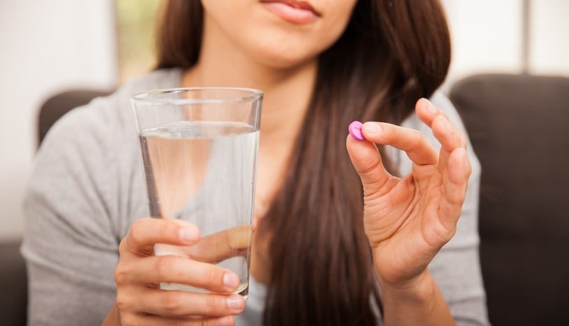 Woman with a glass of water and a pill going to take it.
