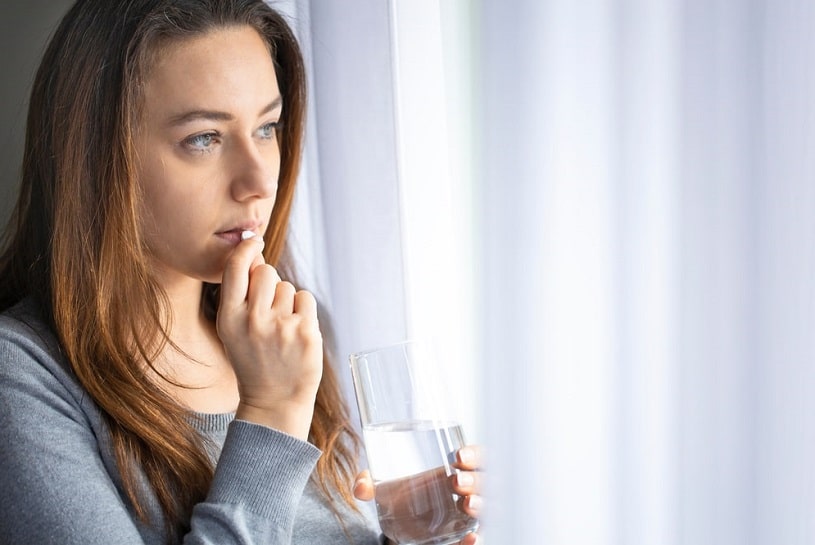 Worried young woman taking Oxycodone and looking in the window.