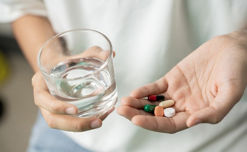 Man holding pills and a glass of water planning to stop taking them.